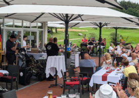 Viele Menschen sitzen an den Tischen der Gastronomie eines Golfplatzes