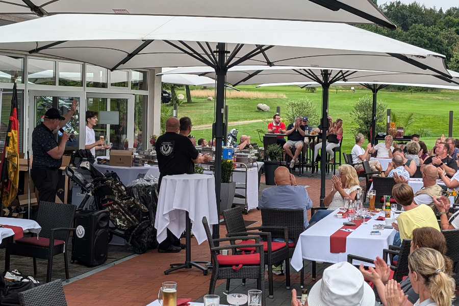 Viele Menschen sitzen an den Tischen der Gastronomie eines Golfplatzes