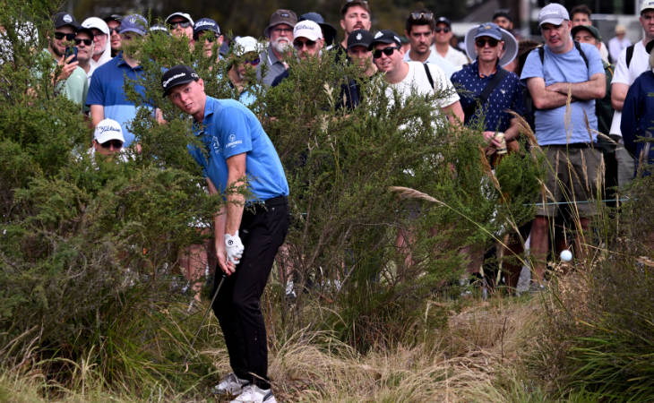 Ryggs Johnston schlägt einen Golfball aus dem Rough, hinter ihm stehen Zuschauer.