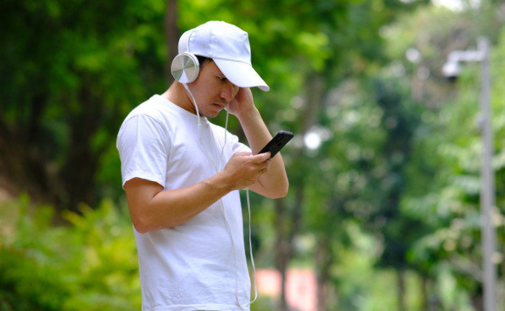 Ein Mann mit weißem Tshirt und weißer Cappie hört via Handy Musik